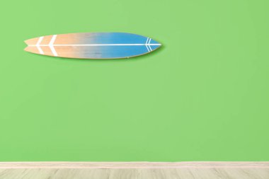 Odanın yeşil duvarında tahta sörf tahtası asılı.