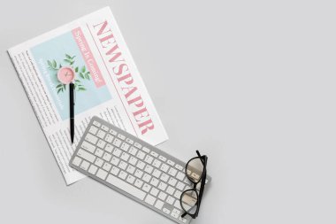 Kalem, bilgisayar klavyesi ve arka planda gözlüklü gazete