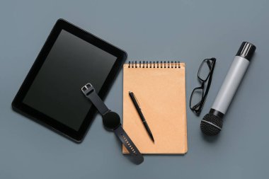 Koyu arkaplanda not defteri, gözlük ve mikrofon olan tablet bilgisayar