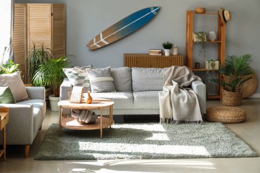 Sörf tahtası, ev bitkileri ve kanepelerle aydınlık oturma odasının içinde.