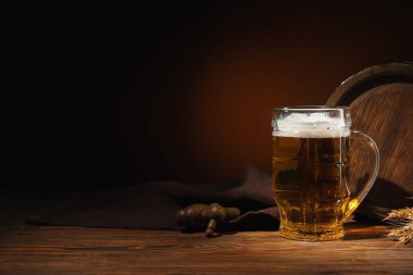 Bir kupa soğuk bira ve ahşap fıçı masanın üstünde, arka planda.