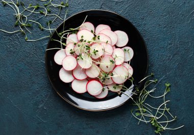 Dilimlenmiş taze turp ve mavi grunge arka planda mikroyeşillikler.