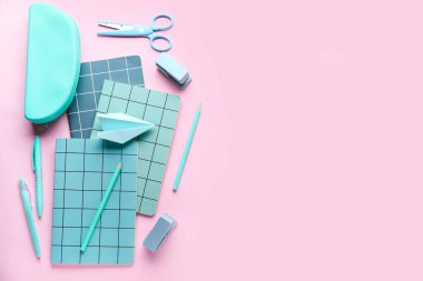 Kırtasiye malzemeleri ve pembe arka planda kağıt uçak kompozisyonu