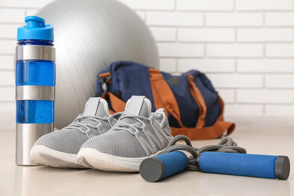 Sports water bottle with sneakers and skipping rope in gym, closeup