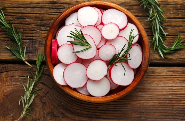 Stock image Bowl with slices of fresh radish and rosemary on wooden table