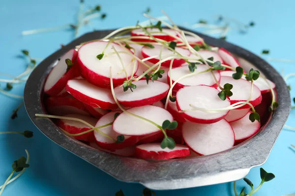 Bowl with sliced radish and microgreens on blue background