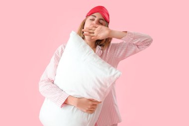 Pembe arka planda yastıklı pijamalı genç bir kadın.