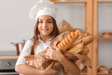 Little baker with tasty baguettes in kitchen