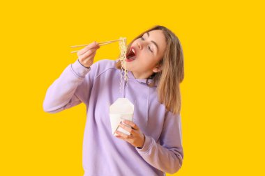 Sarı arka planda Çin eriştesi yiyen genç bir kadın.