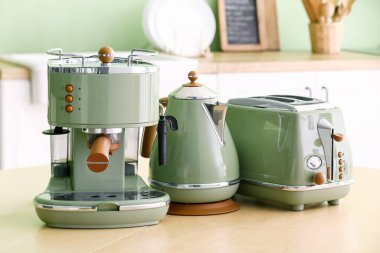 Elektrik ısıtıcısı, kahve makinesi ve ekmek kızartma makinesi mutfaktaki ahşap masada.