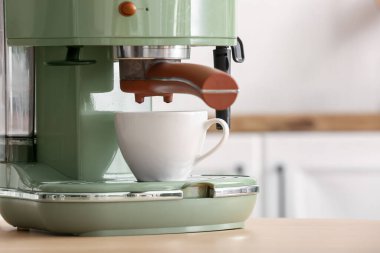 Mutfaktaki ahşap masada fincanı olan modern kahve makinesi.