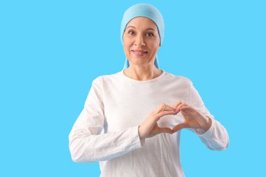 Kemoterapiden sonra olgun bir kadın elleri mavi arka planda kalp yapıyor.