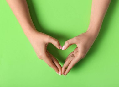 Yeşil arka planda elleriyle kalp yapan bir kadın.