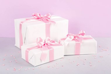 Güzel fiyonklu hediye kutuları ve pembe arka planda konfeti.