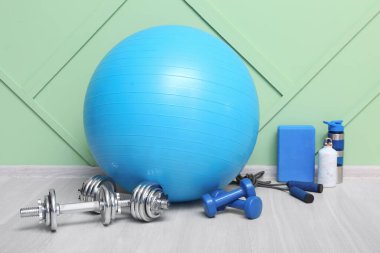 Spor aletleri spor salonunda yeşil duvarın yanında dambıllı.