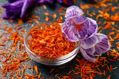 Bir kase kurumuş safran iplik ve güveç çiçekleri siyah masada.
