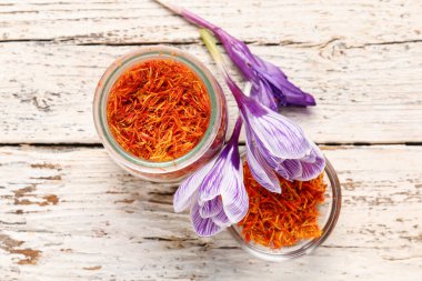 Kavanoz ve bir kase kurumuş safran iplik ve beyaz ahşap masa üzerinde crocus çiçekleri.
