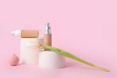 Dekoratif sıva podyumları, makyaj vakfı şişeleri ve pembe arka planda lale çiçeği.