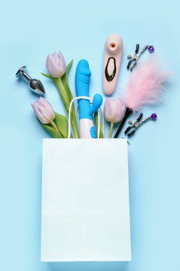 İçinde seks oyuncakları ve mavi arka planda laleler olan kağıt torba.