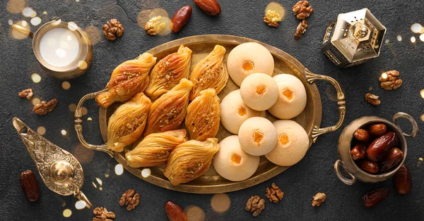 Tray with tasty Eastern sweets and Arabic lamps on dark background