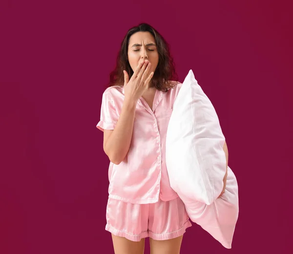 若いですブルネット女性でパジャマで枕Yawningオンピンクの背景 — ストック写真