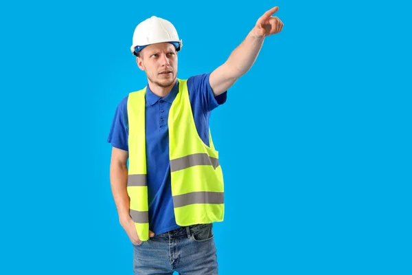 Trabalhador Masculino Colete Chapéu Duro Apontando Para Algo Fundo Azul — Fotografia de Stock