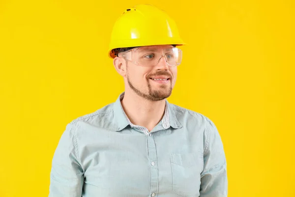Male carpenter in safety goggles on yellow background