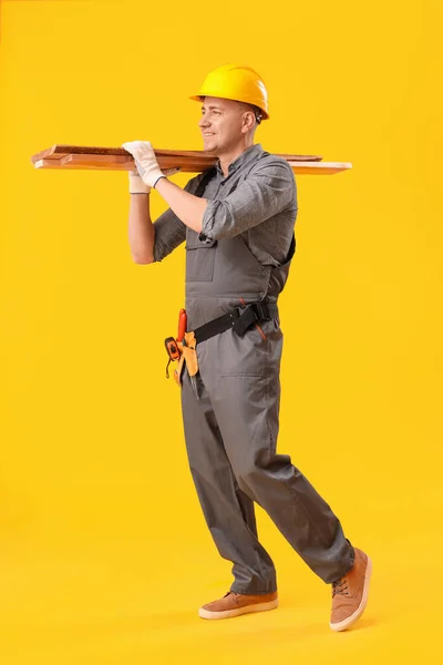 Mature carpenter with wooden planks on yellow background