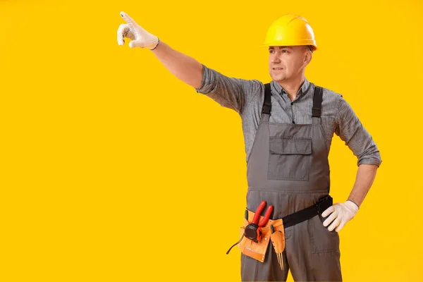 Mature carpenter pointing at something on yellow background