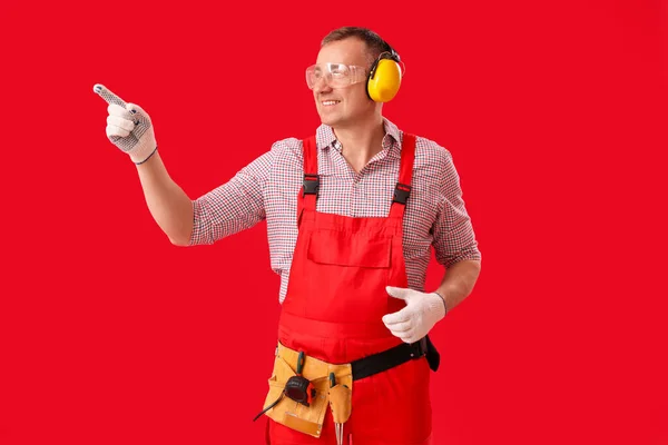 Mature Carpenter Hearing Protectors Pointing Something Red Background — Stock Photo, Image