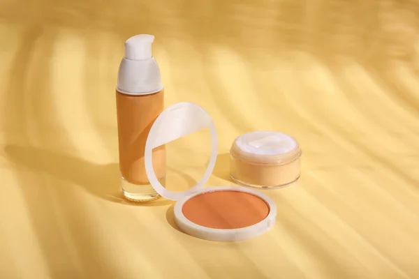 Concealer, liquid foundation and makeup powder on color background