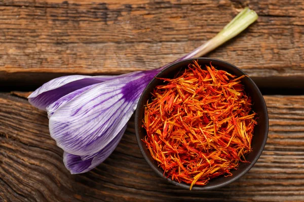 stock image Bowl of dried saffron threads with crocus flower on wooden table