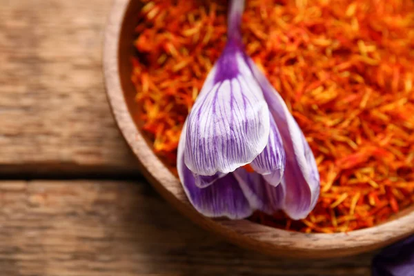 Bowl of dried saffron threads with crocus flowers on wooden table
