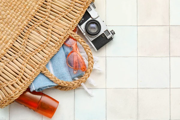 stock image Composition with camera, sunglasses, bottle of sunscreen and towel in wicker bag on tiled background