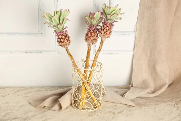 Vase with decorative pineapples on table near light wall