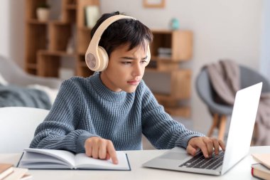 Little boy in headphones with book using laptop at home