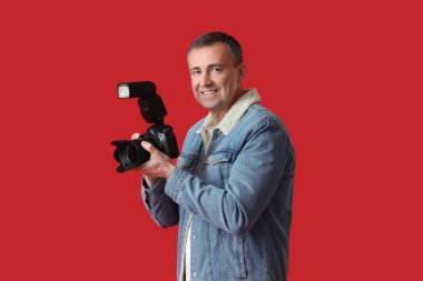 Kırmızı arka planda profesyonel kamerası olan olgun bir fotoğrafçı.