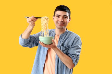 Sarı arka planda bir kase Çin eriştesi olan genç adam.