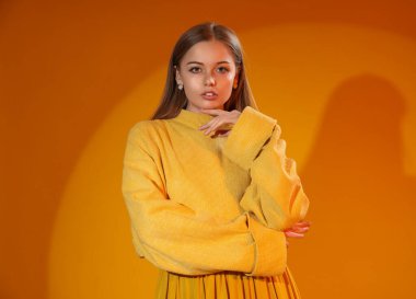 Fashionable young woman in knitted sweater on orange background