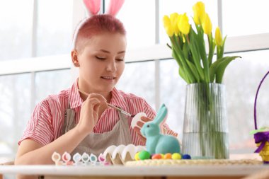 Mutfaktaki masada Paskalya yumurtası boyayan genç bir kadın.