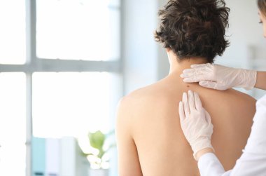 Dermatolog klinikte genç adamın sırtındaki beni inceliyor.