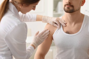 Dermatolog klinikteki genç adamın benlerini inceliyor.