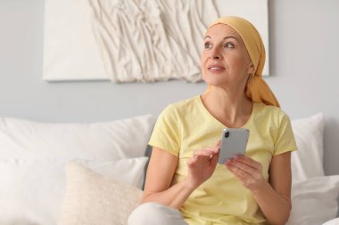 Kemoterapiden sonra yatak odasında cep telefonu kullanan olgun bir kadın.