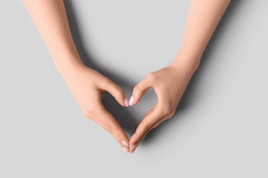 Gri arka planda elleriyle kalp yapan bir kadın.