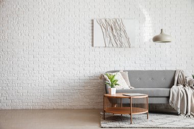 Beyaz tuğla duvarın yanında modern dizüstü bilgisayarı olan gri kanepe ve kahve masası.