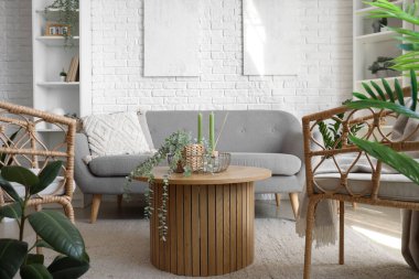 Parlak oturma odasında aroma mumları ve çiçekli kahve masası.