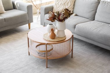 Oturma odasında kurutulmuş protea çiçekleri olan rahat gri kanepe ve kahve masası.