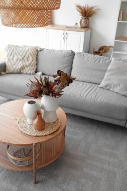 Oturma odasında kurutulmuş protea çiçekleri olan rahat gri kanepe ve kahve masası.
