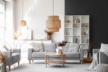 Parlak oturma odasının içinde, kahve masasında gri kanepeler ve vazolar var.