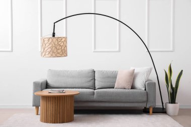 Modern oturma odasının içinde rahat gri kanepe, sehpa ve lamba var.